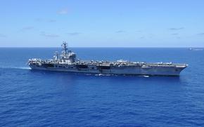 An aircraft carrier sails in open ocean with the horizon in the background.